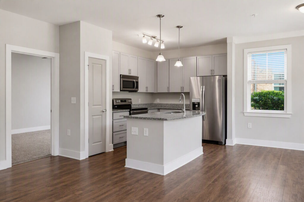 Modern kitchen with white cabinets, stainless steel appliances, a granite island, and wood flooring. Theres a window letting in natural light and an open doorway leading to a carpeted room.